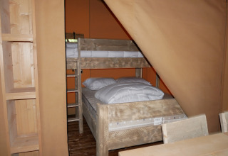 Binnenzijde van een safaritent met houten stapelbed, open kasten en rustieke houten inrichting.