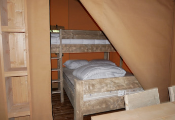 Interior de una tienda safari con literas y muebles rústicos de madera en una zona para dormir.