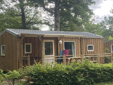 Træhytte i naturskønne omgivelser hos Cottage Zen glamping, med veranda og grønne træer omkring.