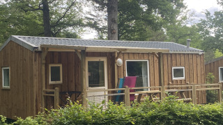 Houten cottage bij Cottage Zen glamping, met veranda en omgeven door groene bomen en natuur.