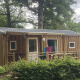 Træhytte i naturskønne omgivelser hos Cottage Zen glamping, med veranda og grønne træer omkring.