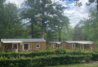 Drie houten hutten in een bosrijke omgeving onder blauwe lucht, gefotografeerd bij glamping Cottage Zen.
