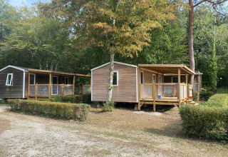 To træhytter med terrasser foran, omgivet af buske og træer på et glampingsted kaldet Cottage Zen.