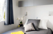 Modernes Glamping-Schlafzimmer im Cottage Zen mit grauer Bettwäsche, gelben Handtüchern und Fenster.
