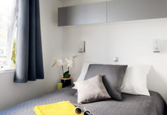 Moderne glamping Cottage Zen slaapkamer met grijs bedlinnen, gele handdoeken en raam met gordijnen.
