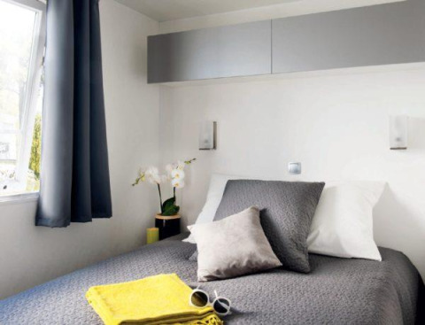 Dormitorio moderno de glamping Cottage Zen con ropa de cama gris, toallas amarillas y ventana.