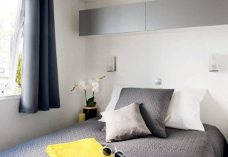 Modern glamping Cottage Zen bedroom with grey bedding, yellow towels, and window with dark curtains.
