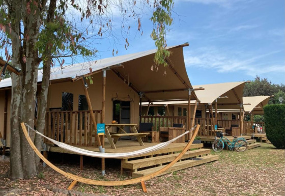 Tienda safari Wood Lodge con sanitarios privados, terraza, hamaca y bicicleta bajo cielo azul.