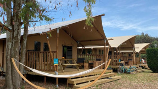 Tienda safari Wood Lodge con sanitarios privados, terraza, hamaca y bicicleta bajo cielo azul.