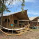 Safari-Zelt Wood Lodge mit Sanitärbereich, Terrasse, Hängematte und Fahrrad unter blauem Himmel.