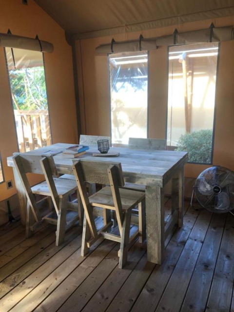 Interior de tienda safari con mesa de madera, cuatro sillas y ventilador en Village Seasonova Bassin d'Arcachon, Francia.