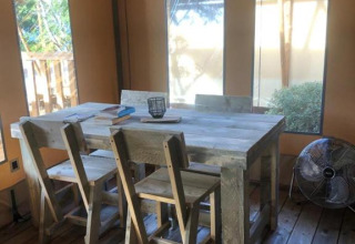 Interior de tienda safari con mesa de madera, cuatro sillas y ventilador en Village Seasonova Bassin d'Arcachon, Francia.