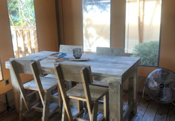 Interior de tienda safari con mesa de madera, cuatro sillas y ventilador en Village Seasonova Bassin d'Arcachon, Francia.