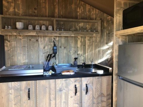 Cozy safari tent kitchenette at Village Seasonova Bassin d'Arcachon with sink, fridge and rustic wood shelving.