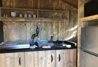 Cozy safari tent kitchenette at Village Seasonova Bassin d'Arcachon with sink, fridge and rustic wood shelving.