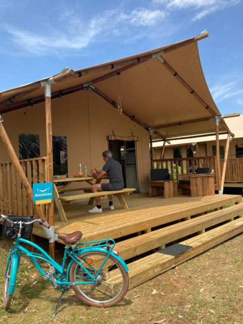 Mann sitzt auf Terrasse eines Safari-Zelts Wood Lodge + Sanitär im Village Seasonova Bassin d'Arcachon, Frankreich.