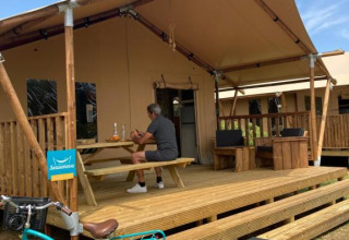 Hombre sentado en la terraza de una tienda safari Wood Lodge + sanitario en Village Seasonova Bassin d'Arcachon, Francia.