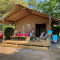 Safari tent genaamd Slow Lodge + badkamer, met twee mensen zittend op de veranda tussen bomen.