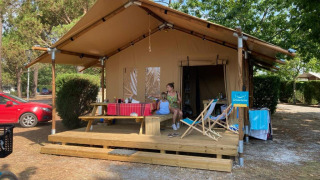 Tenda safari chiamata Slow Lodge + bagno, con due persone sedute sulla veranda tra gli alberi.