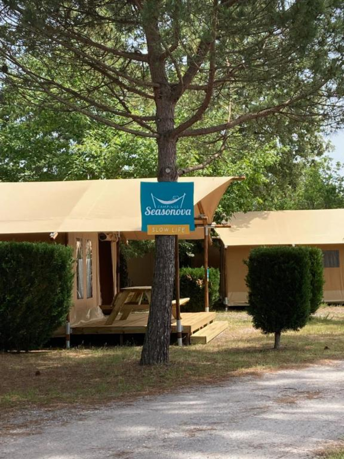 Safari tent bij Slow Lodge + badkamer in Village Seasonova Bassin d'Arcachon, Frankrijk, met boom en bord.