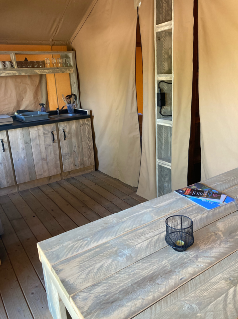 Interieur van een safaritent bij Slow Lodge met houten tafel en keukentje, Village Seasonova Bassin d'Arcachon, Frankrijk.