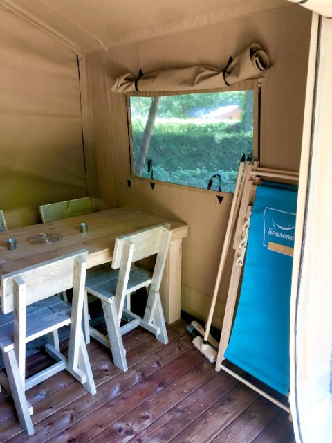 Interno di una tenda safari con sedie e tavolo in legno, grande finestra e sdraio al Village Seasonova Bassin d'Arcachon.