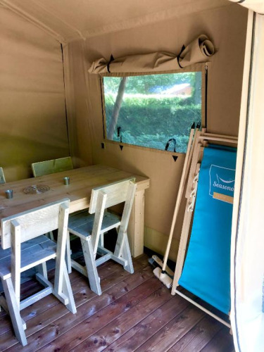 Innenansicht eines Safarizeltes mit Holzmöbeln, Fenster und Liegestuhl im Village Seasonova Bassin d'Arcachon.