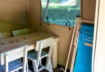 Innenansicht eines Safarizeltes mit Holzmöbeln, Fenster und Liegestuhl im Village Seasonova Bassin d'Arcachon.