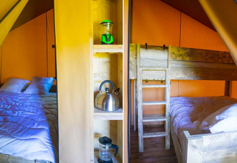 Interior of a safari tent featuring a double bed, bunk bed, and shelves with a lantern, kettle, and coffeepress.