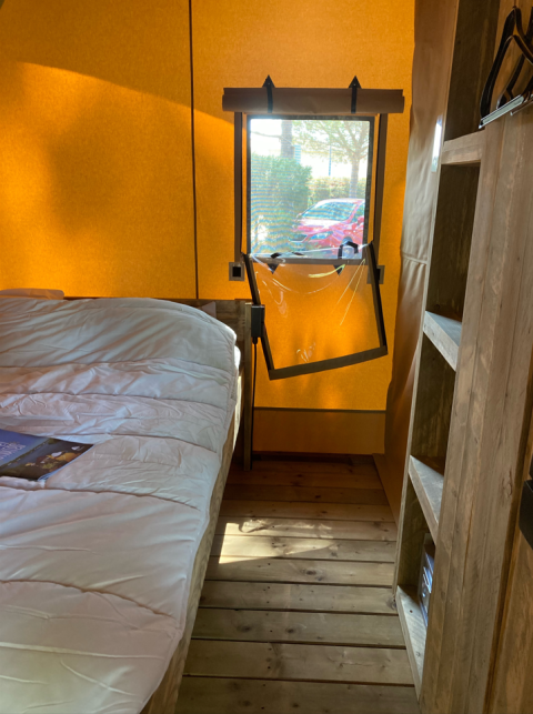 Vista interior de una tienda safari en Slow Lodge con suelo de madera, cama y ventana abierta, en Village Seasonova Bassin d'Arcachon.