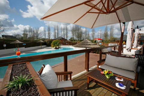 Outdoor seating area with wooden furniture, umbrellas, and pool view at Camping Seasonova Haliotis, Normandy.