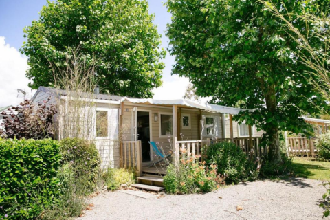 Mobile home at Camping Seasonova Haliotis in Normandy, France, surrounded by lush greenery and tall trees.