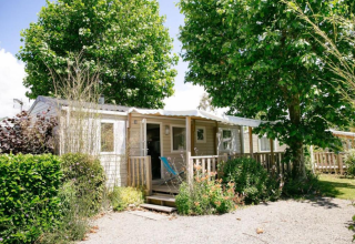 Stacaravan bij Camping Seasonova Haliotis in Normandië, Frankrijk, omgeven door veel groen en grote bomen.
