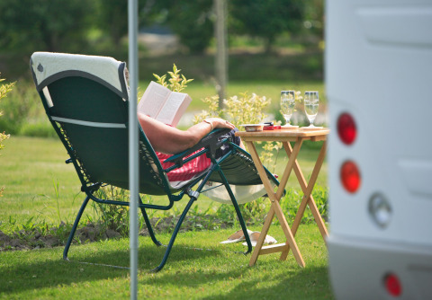 Personne détendue sur une chaise longue lisant un livre à côté d'une table avec verres au camping en Normandie.