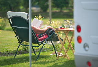 Person entspannt sich auf einem Campingstuhl, liest ein Buch neben einem Tisch mit Gläsern im Park in der Normandie.