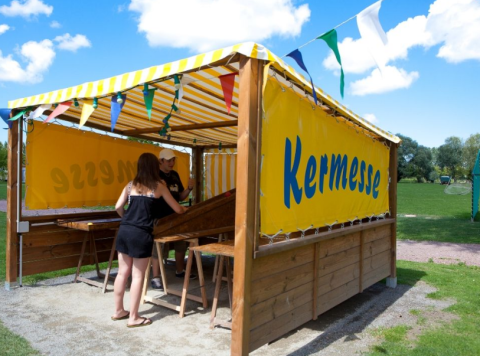 Two people play a fair game under a yellow-striped canopy at Camping Seasonova Haliotis in Normandy, France.