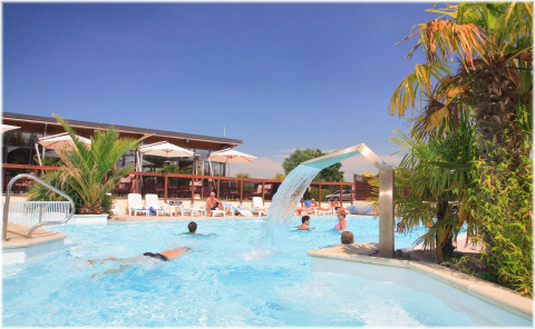 Turistas disfrutan de la piscina con palmeras y cascada en Camping Seasonova Haliotis en Normandía, Francia.