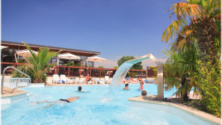 Turistas disfrutan de la piscina con palmeras y cascada en Camping Seasonova Haliotis en Normandía, Francia.
