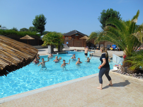 Turistas se divierten en la piscina con animación, rodeados de palmeras en Camping Seasonova Haliotis, Normandía, Francia.