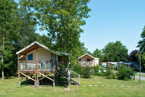 Sistemazione glamping con tende rialzate su terrazze in legno immerse nel verde tra alberi e prato.