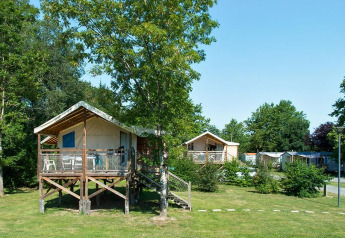 Sistemazione glamping con tende rialzate su terrazze in legno immerse nel verde tra alberi e prato.