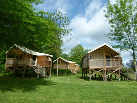 Tres cabañas de madera elevadas en Camping Seasonova Les Plages de Loire, rodeadas de árboles en Francia.