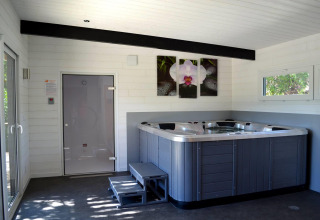 Binnen met jacuzzi en sauna in een lichte ruimte met ramen, moderne inrichting en orchidee aan de muur.