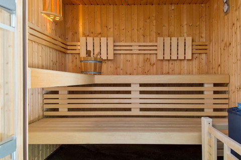 Vista interna di una moderna sauna in legno con panche e secchio al Camping Seasonova Les Plages de Loire.