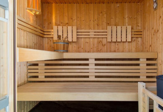 Vista interna di una moderna sauna in legno con panche e secchio al Camping Seasonova Les Plages de Loire.