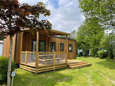 Outdoor view of the Premium Cottage lodge with wooden deck surrounded by green grass and leafy trees.