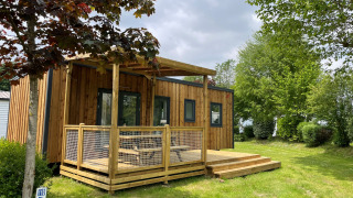 Buitenaanzicht van de Premium Cottage lodge met houten terras, grasveld en omliggende groene bomen.