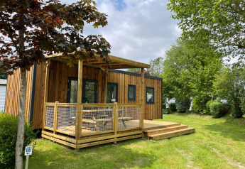 Vue extérieure du lodge Premium Cottage avec terrasse en bois et pelouse, entouré d’arbres feuillus.