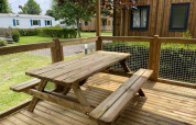 Trætabel og bænk på terrasse ved Premium Cottage, Camping Seasonova Haliotis, omringet af grøn natur.
