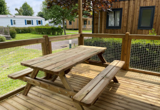 Mesa y bancos de madera en la terraza de Premium Cottage en Camping Seasonova Haliotis, rodeada de naturaleza.